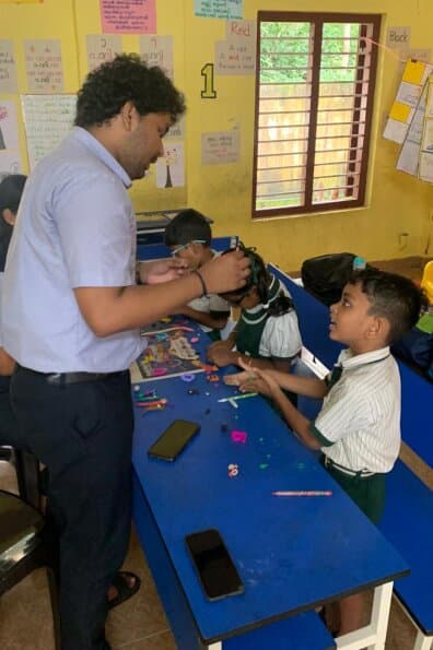 A faculty member leaning over a desk covered in craft materials, helping a child with a hands-on activity.