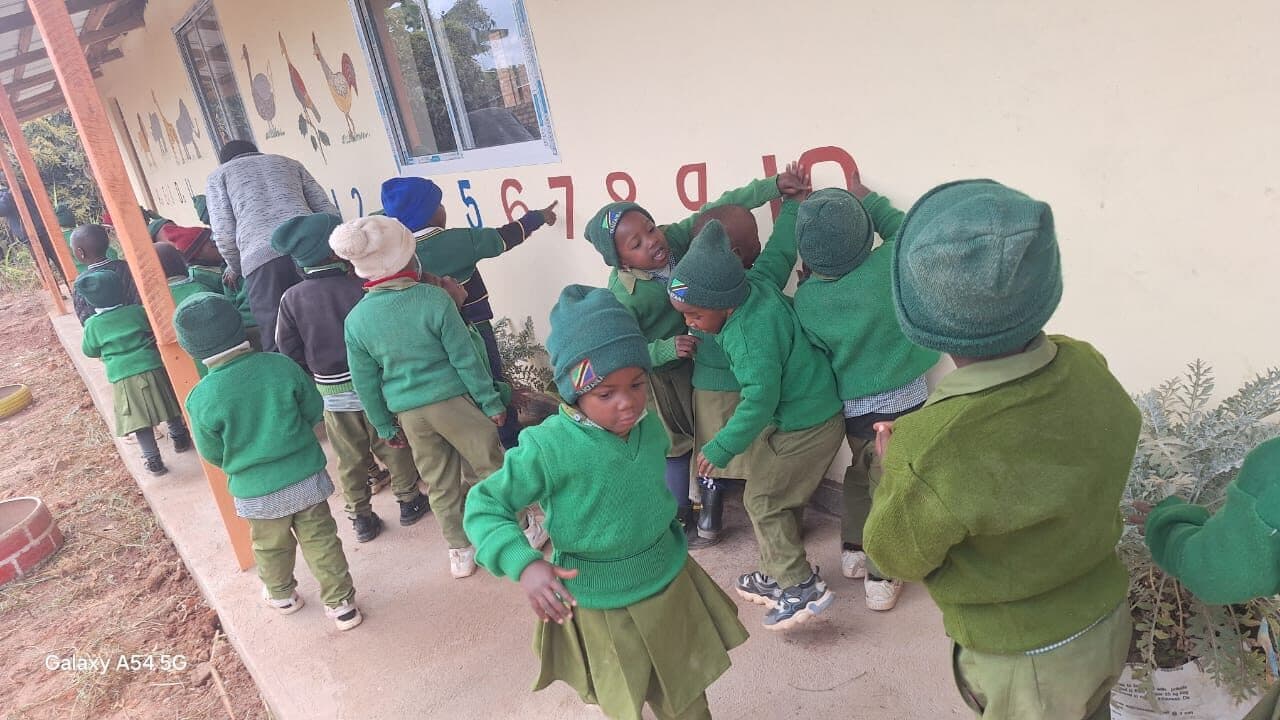 A group of children spread along the veranda wall, some pointing at the painted numerals, one turning to face the camera.