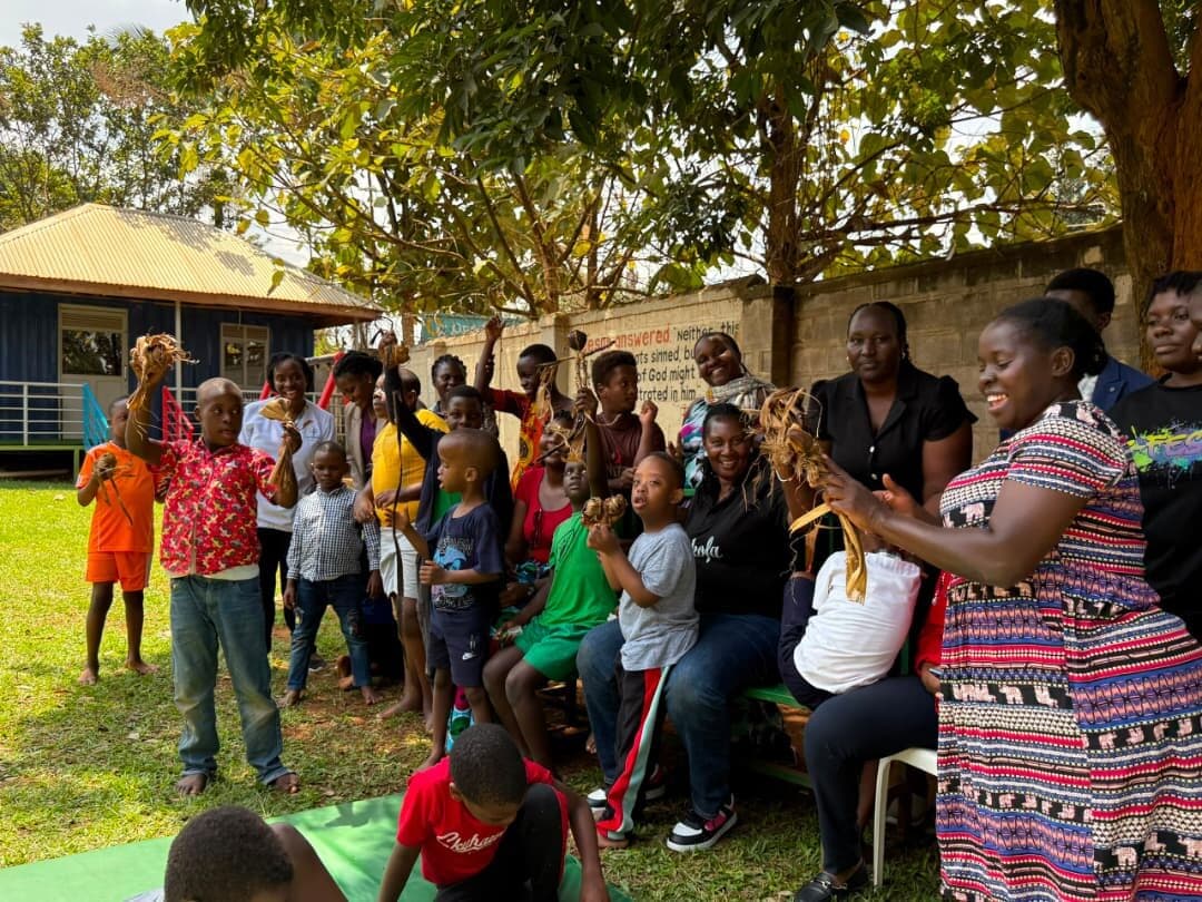 Learners and teachers under a tree raising their banana fibre creations above their heads.